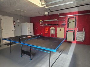 A ping pong table in a room with a red wall, a white door, and a clock.