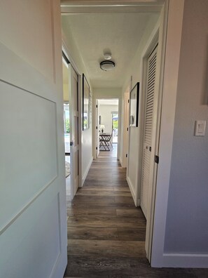 A hallway with wooden flooring, white walls, and doors leading to a balcony with outdoor furniture.