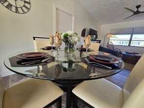 A dining area with a round glass table, chairs, and a clock on the wall.