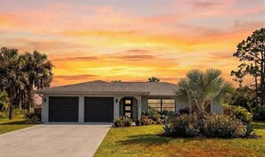 A residential house with a garage, surrounded by well-maintained landscaping, including palm trees and shrubs.