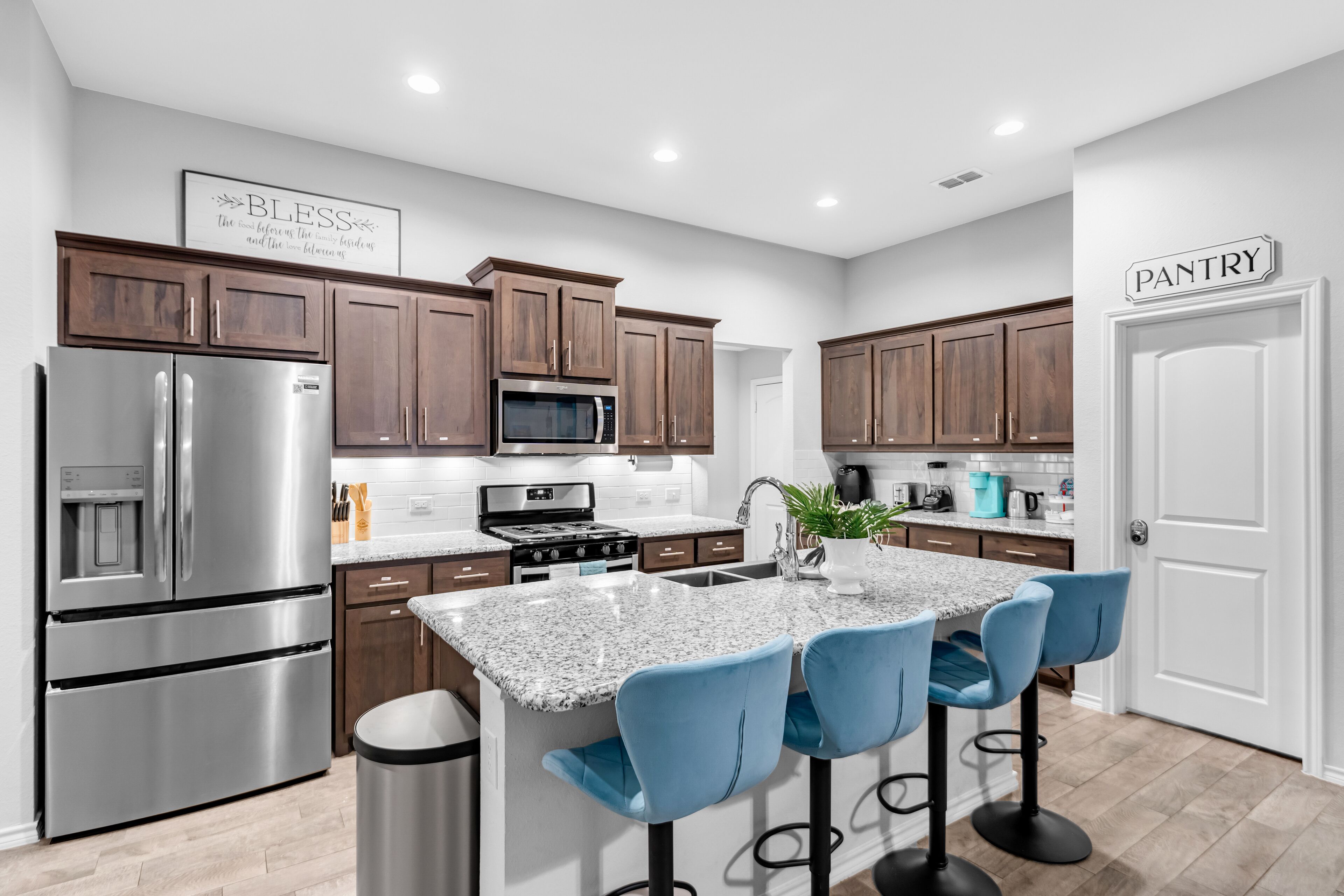 Una cocina moderna con electrodomésticos de acero inoxidable, armarios de madera y una isla de granito con taburetes de bar.