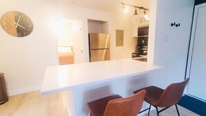 A modern kitchen with a white countertop, stainless steel appliances, and two brown chairs. -  ★Cozy Apt Near SLU Hospital & Other Major Hospitals ★ (St. Louis)