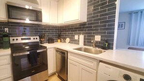 A modern kitchen with white cabinets, a black tiled backsplash, stainless steel appliances, and a dishwasher. -  ★Cozy Apt Near SLU Hospital & Other Major Hospitals ★ (St. Louis)