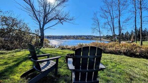 Two Adirondack chairs facing a body of water with a clear sky. - Beachfront Cottage with Fire Pit in Watering Cove (Gouldsboro)