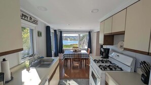 A compact kitchen with a dining area, a view of the outdoors, and a sign reading "HAPPY PLACE". - Beachfront Cottage with Fire Pit in Watering Cove (Gouldsboro)