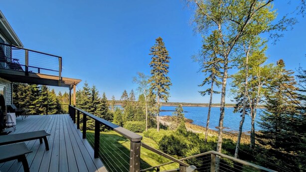 A wooden deck with a railing, overlooking a lake and forest. - Oceanfront Cottage w/ Fire Pit & Sunset Deck (Gouldsboro)