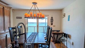 A dining area with a table, chairs, a chandelier, and a view of the ocean. - Oceanfront Cottage w/ Fire Pit & Sunset Deck (Gouldsboro)