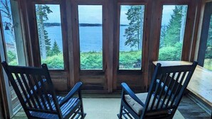 A cabin with large windows offering views of a lake and forest. - Oceanfront Cottage w/ Fire Pit & Sunset Deck (Gouldsboro)