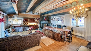 Una sala de estar acogedora y rústica con techo de madera, chimenea, comedor y candelabro.