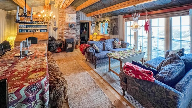 Un interior acogedor y rústico con techo de madera, chimenea, un conjunto de sofás y una mesa de comedor.