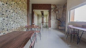 A dining area with wooden tables and chairs, a wall of stacked logs, and a view through a doorway to another room. - Jepun Guest House (Mataram)