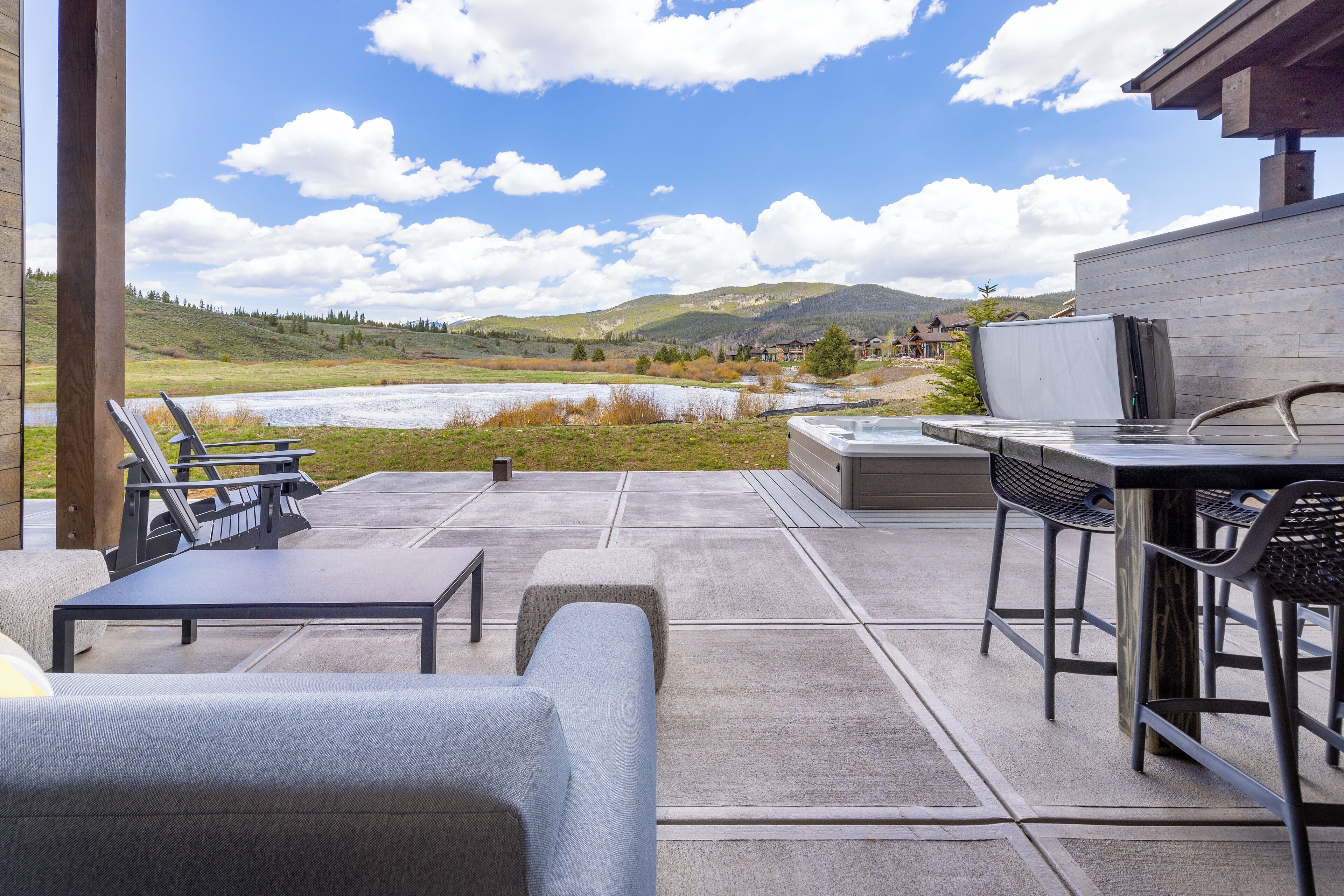 Une terrasse extérieure offrant une vue sur un lac et des collines, équipée d’un barbecue, de sièges et d’une table.