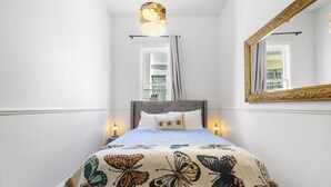 A bedroom with a bed, a large mirror, and a window with curtains. - Worldwide Backpackers Limited (Wellington)