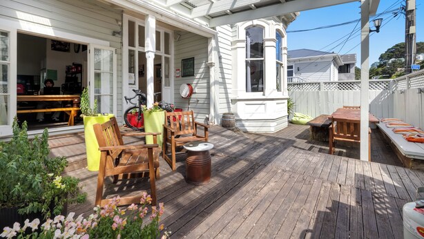 A covered patio with wooden furniture, a bicycle, and a white fence. - Worldwide Backpackers Limited (Wellington)