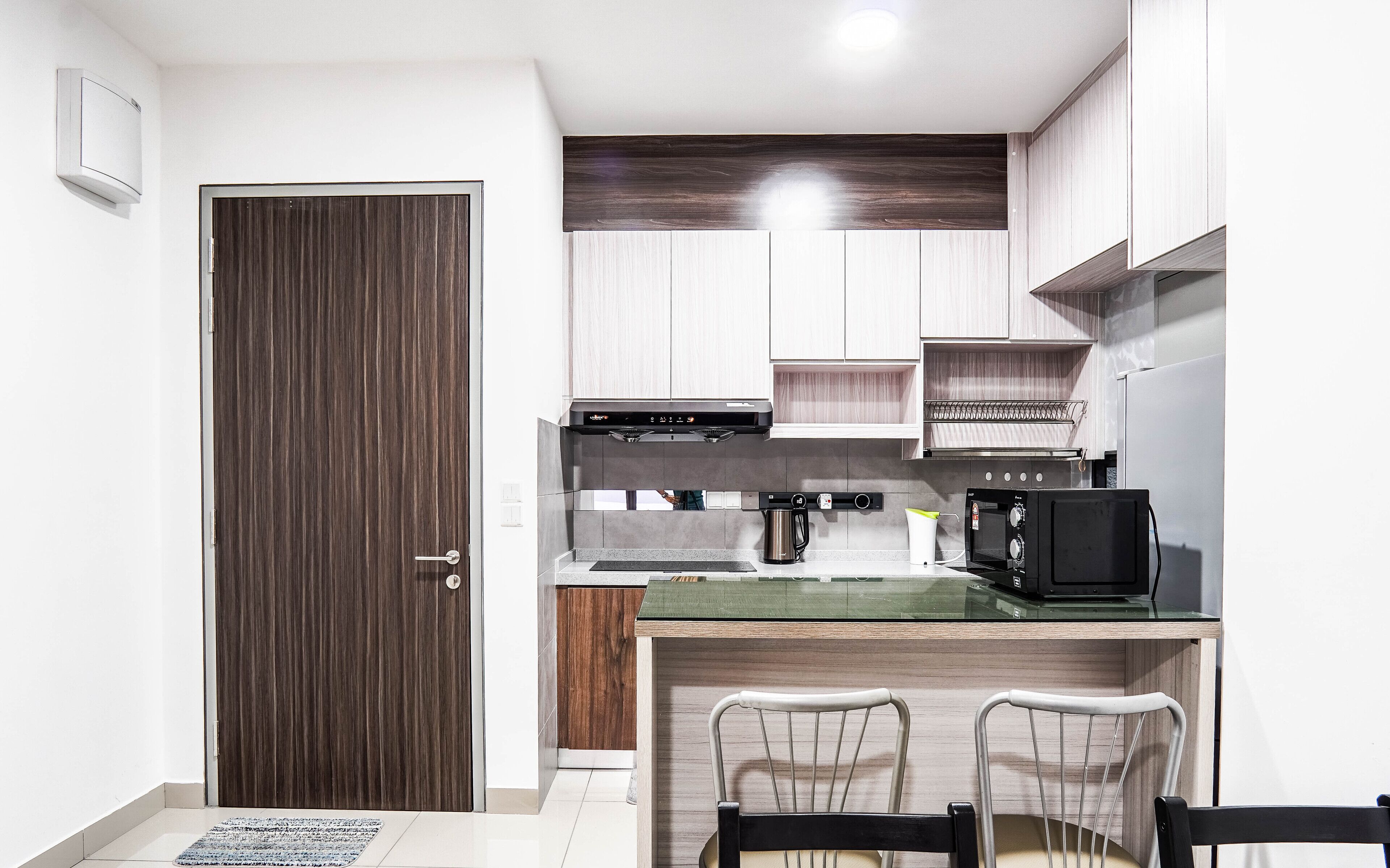 A compact kitchen with a wooden door, a built-in oven, a coffee maker, and a small dining area with two chairs.