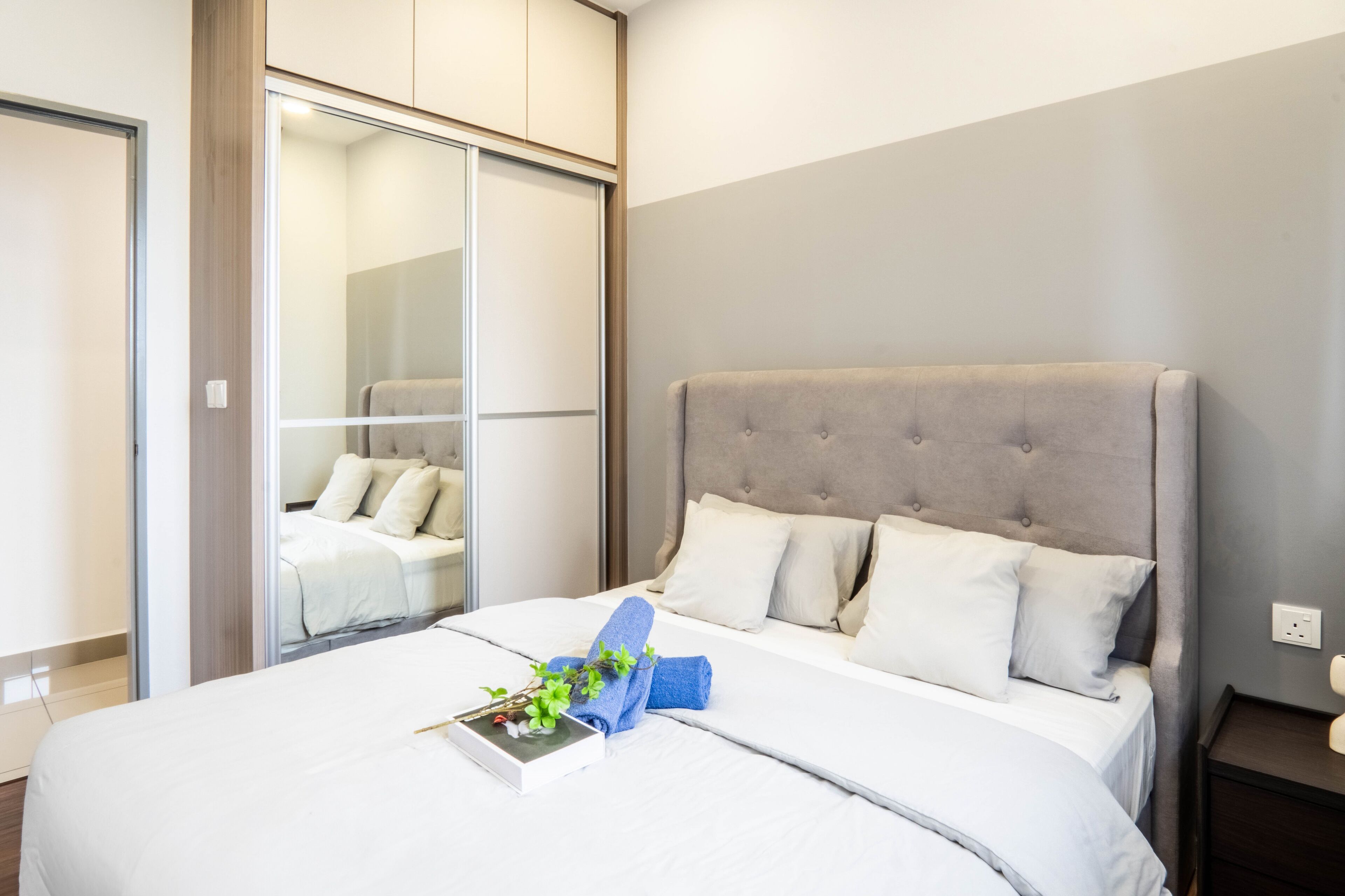 A modern bedroom with a large bed, a wardrobe with a mirror, and a bedside table.
