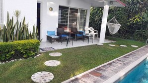 Une terrasse avec une table et des chaises, un petit jardin agrémenté d’un chemin de pierres, et une piscine.