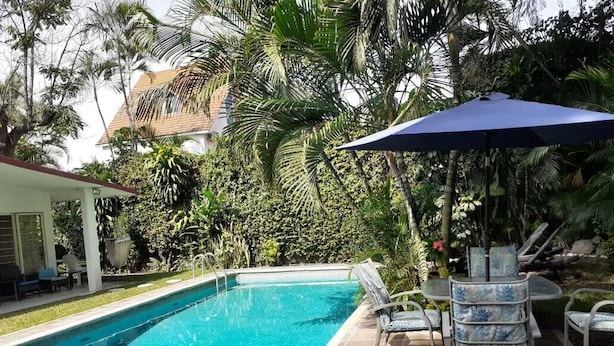 Une piscine dotée d’une terrasse carrelée, entourée d’une végétation luxuriante et agrémentée d’un espace salon abrité.