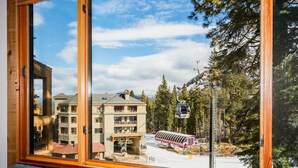 Une vue depuis une fenêtre d’un bâtiment, avec un télésiège et les arbres environnants.