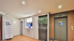 Un vestíbulo de hotel con una recepción, una planta en la pared y un ascensor.