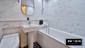 Un baño moderno con una bañera blanca, un lavamanos y un inodoro. Hay un espejo sobre el lavamanos y un perchero sobre la bañera.