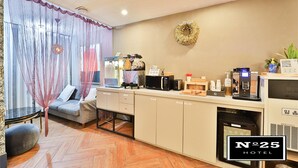 Habitación de hotel con kitchenette, sofá, cafetera y un arreglo decorativo en la pared.