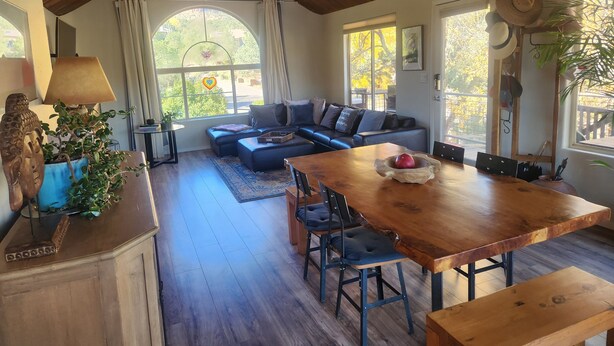 A spacious living area with a wooden ceiling, a large wooden dining table, and a cozy seating area with a sofa and chairs.