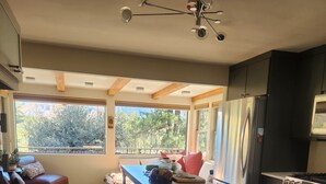 A modern kitchen with wooden flooring, a dining area with a table and chairs, and a view of trees through large windows.