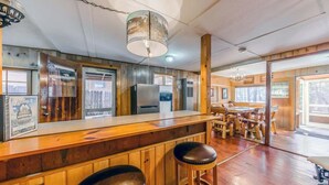 A wooden bar area with stools, a refrigerator, and a hanging light fixture.