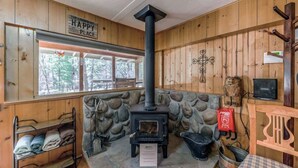 A cozy room with a stone wall, a black wood-burning stove, a window with a view of trees, a metal rack with towels, and a sign that says 'The Cabin is My Happy Place.'