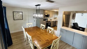 Una cocina moderna con electrodomésticos de acero inoxidable, una mesa de comedor de madera y armarios de tonos claros.