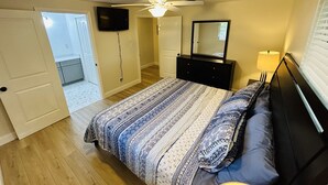 Un dormitorio con cama, cómoda, espejo, ventilador de techo y televisor montado en la pared.