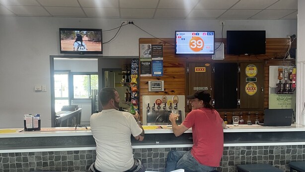 Eine Bar mit zwei Gästen am Tresen, einem an der Wand befestigten Fernseher und einer digitalen Anzeige, die die Zahl 39 zeigt.