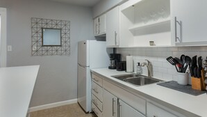 A modern kitchen with white cabinets, a built-in refrigerator, a coffee maker, and a sink with a knife block. - Montrose Svelte Studio! Medical Center 47 (Houston)