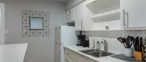 A modern kitchen with white cabinets, a built-in refrigerator, a coffee maker, and a sink with a knife block.