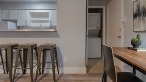 A modern kitchen with white cabinets, a wooden dining table, and bar stools. - Montrose Svelte Studio! Medical Center 47 (Houston)