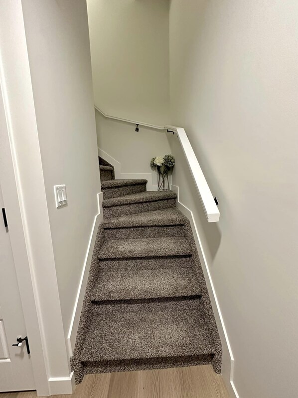 A staircase with carpeted steps and white handrails, leading to a landing with a white wall and a small vase with flowers.