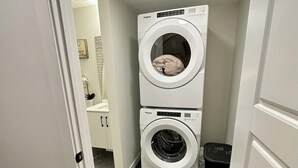 A laundry room with two stacked Whirlpool washers and dryers, a black trash bin, and a tiled floor. - New, fresh, affordable, homey, 10 mins to the Edmonton Intl Airport. (Edmonton)