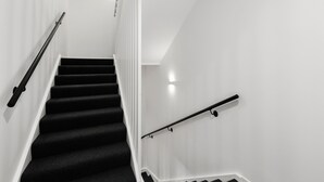 Una escalera con peldaños cubiertos de moqueta negra y paredes blancas, con barandillas a ambos lados.