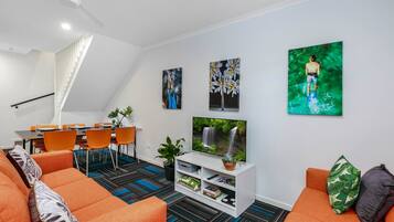 A modern living room with orange sofas, a white entertainment unit, and artwork on the walls.
