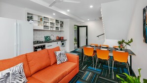 Cocina moderna con armarios blancos, un refrigerador blanco y una zona de comedor con sillas naranjas y una mesa negra.