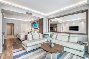 A modern hotel room with a large bed, a sofa, a coffee table, and a TV.