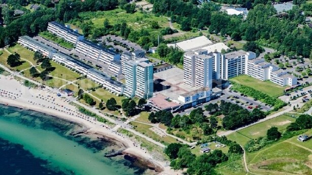 An aerial view of a coastal hotel complex with multiple buildings, a beach, and surrounding greenery.