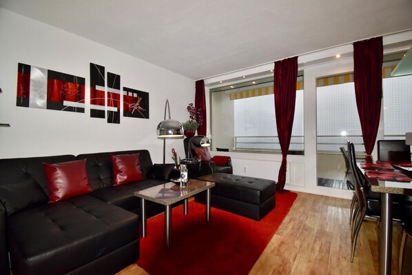 Un salon moderne avec un canapé noir, des coussins rouges, une table basse et un coin repas comprenant une table et des chaises.
