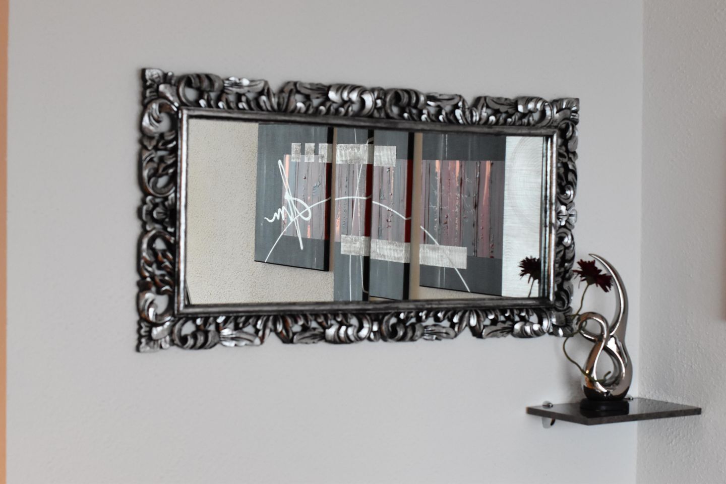 Een spiegel met een sierlijk zilveren frame, bevestigd aan een muur.