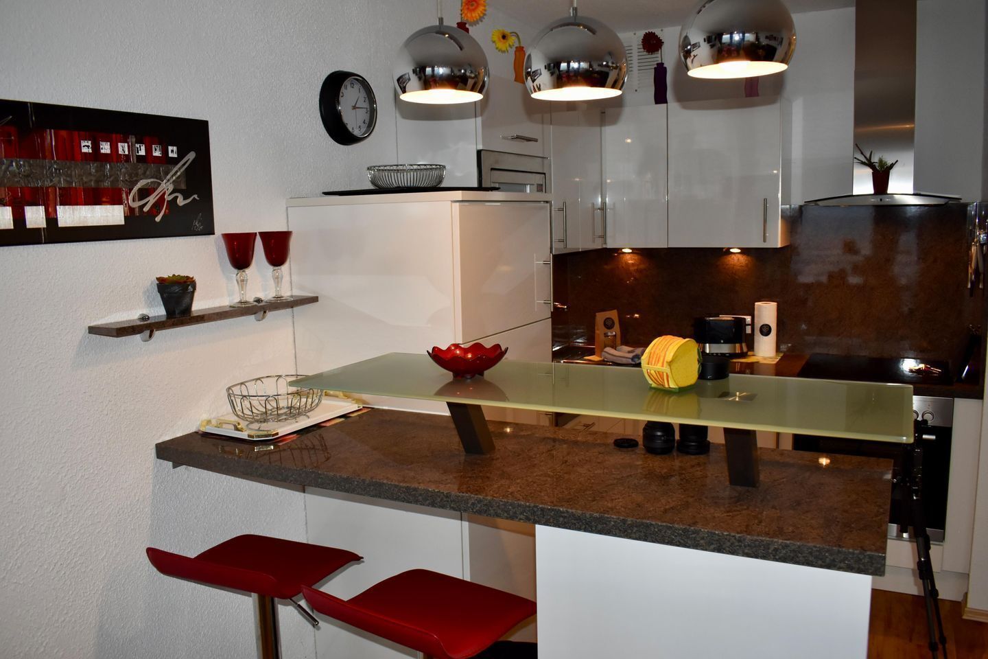 Una cucina moderna con isola centrale, mobili bianchi e sgabelli da bar rossi.
