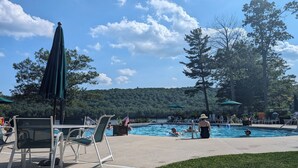 Un área de piscina con sillones de descanso y sombrillas, rodeada de árboles y un paisaje montañoso.