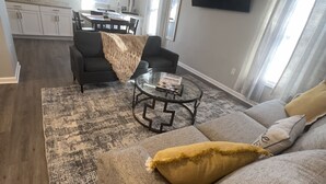 Ein modernes Wohnzimmer mit einer Eckcouch, einem Couchtisch und einem Essbereich im Hintergrund.