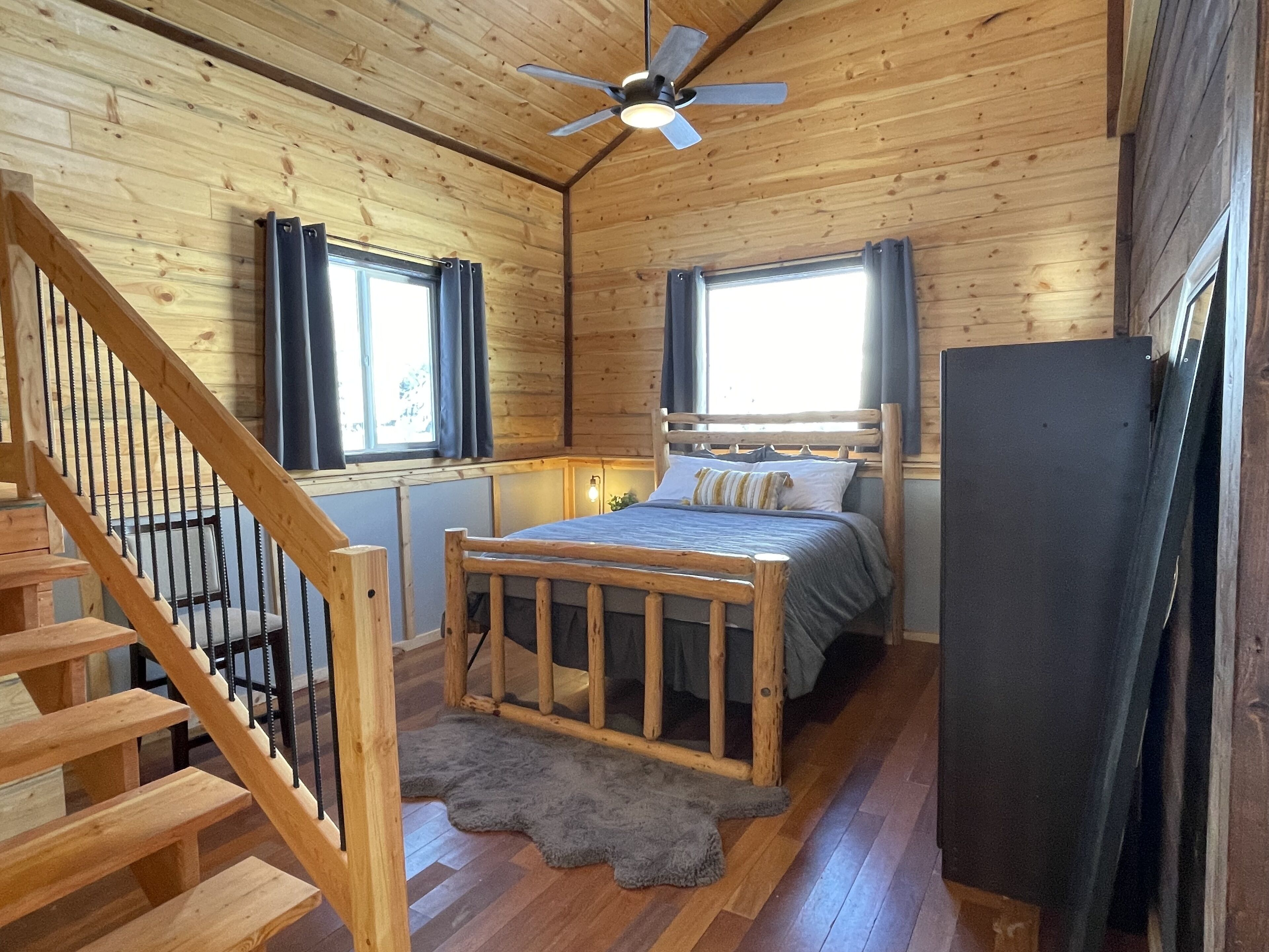 Une pièce dans une cabane en bois, comprenant un lit, un ventilateur de plafond et un escalier.