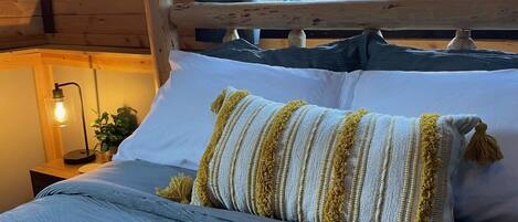 Una cama con cabecera de madera, almohadas blancas y azules, y una almohada rayada con flecos.
